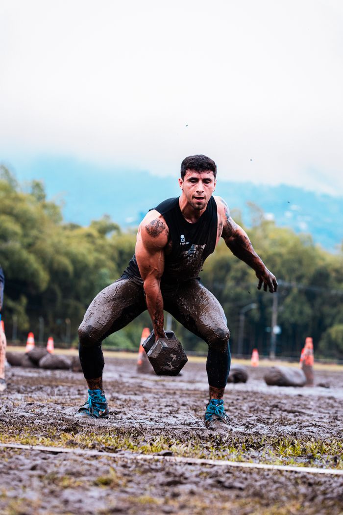 Man performing intense weightlifting during muddy outdoor fitness event.